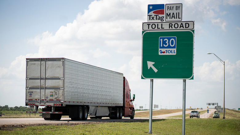 Sign for Texas SH 130 in the foreground with a semi-truck driving in the background.