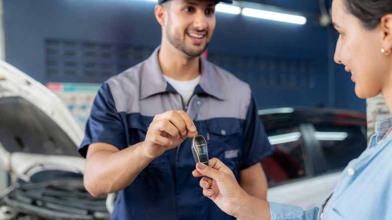 Auto technician handing key to car owner inside repair shop.