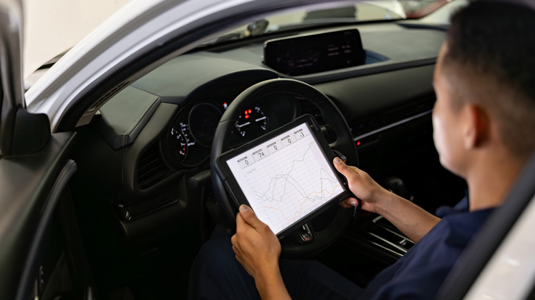 View of mechanic sitting in car diagnosing problems with tablet computer.