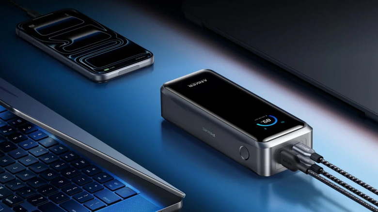An Anker powerbank in use, placed next to a laptop and an smartphone.