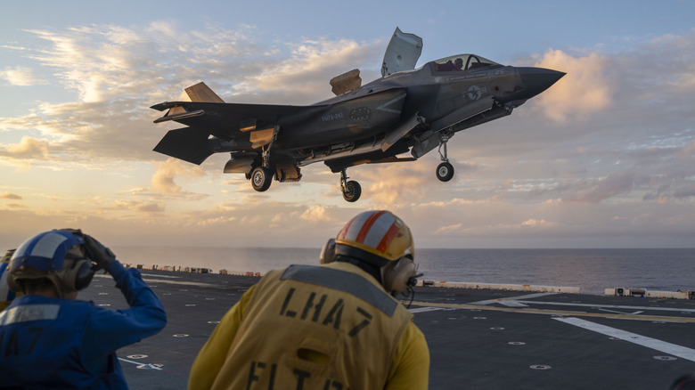 Sailors watch as an F-35B Lighting II lands on a flight deck.