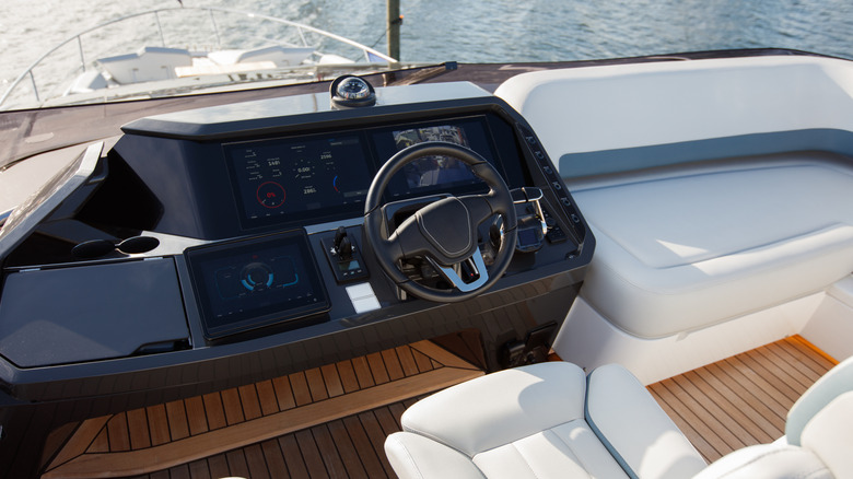 Motorboat cockpit showing steering wheel, infotainment display, and white seats.