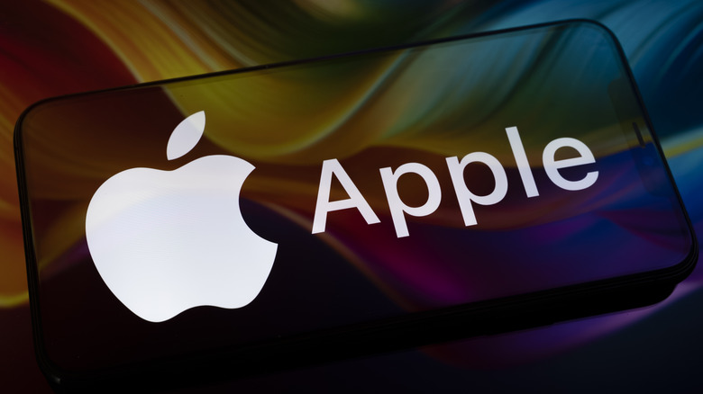 The Apple logo appears on a smartphone screen placed on a reflective surface