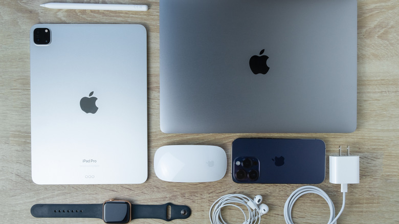 A MacBook, an iPad, an iPhone, an Apple Pencil, a Magic Mouse, an Apple Watch, and a few other Apple devices kept on a wooden table