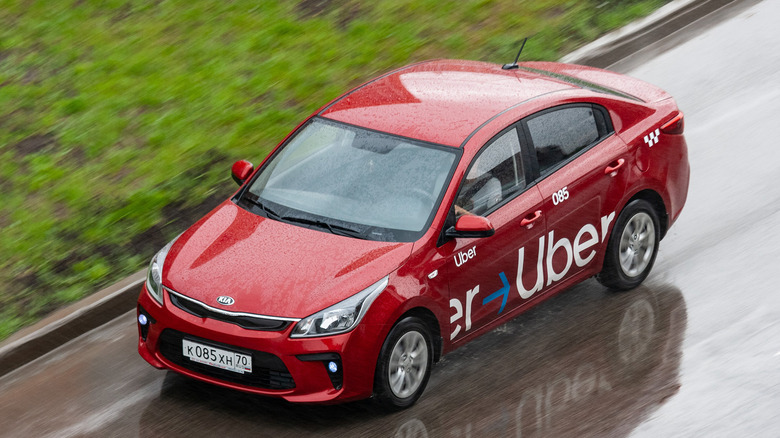 A red car with Uber branding driving along a road.