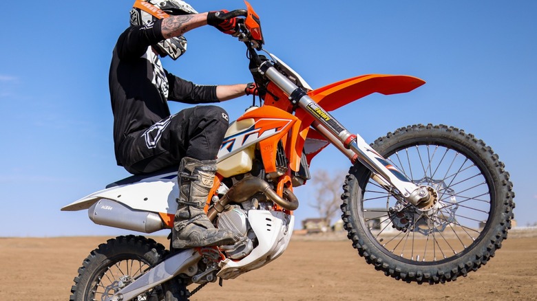 Orange KTM bike on a sandy terrain with the rider doing a wheelie