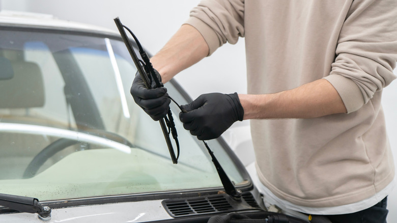 person wearing black latex gloves installing windshield wipers on a car
