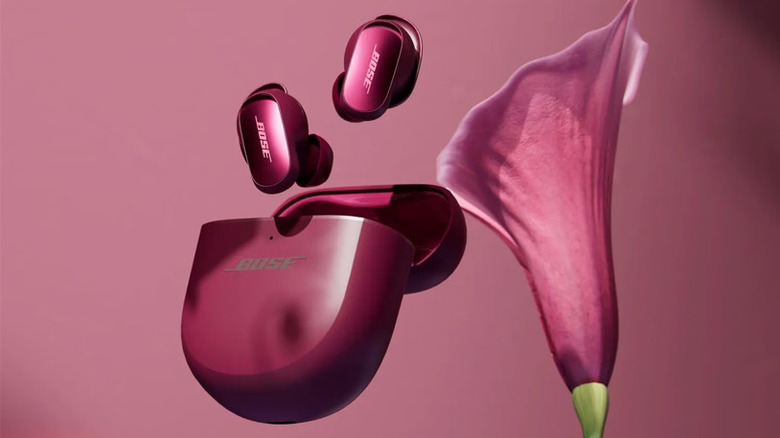 A pair of deep plum Bose QuietComfort Ultra Earbuds with a lily.