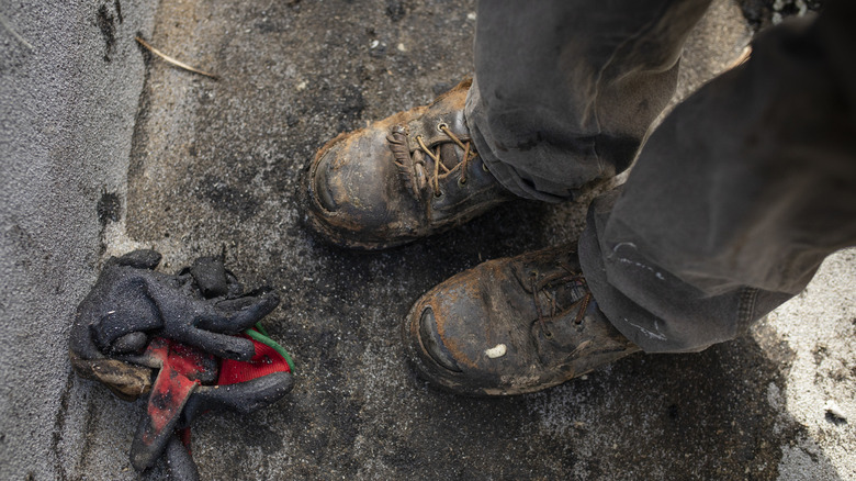 A close-up of someone wearing dirty work boots near work gloves