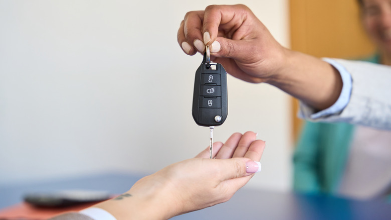 Close up of two hands belonging to two different people. One hand is handing the other, a set of car keys.