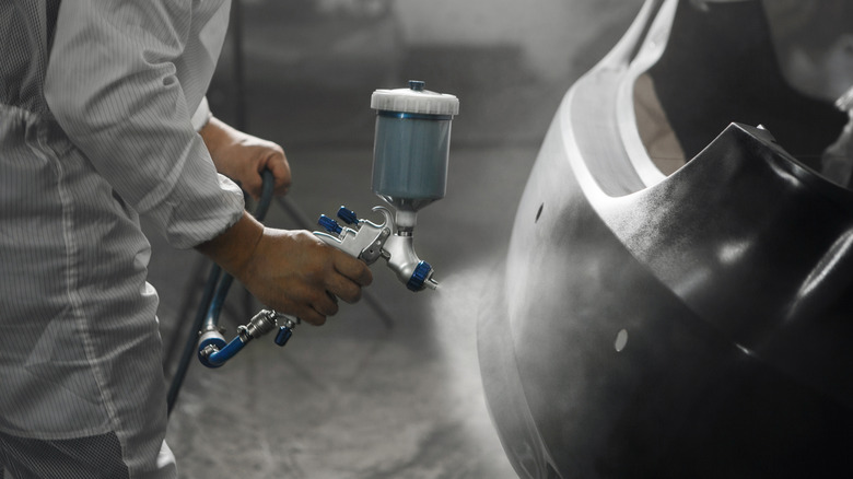 A person using a paint gun to apply primer to a vehicle's rear bumper