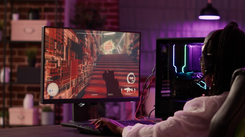 PC gamer playing shooter at desk with desktop and monitor