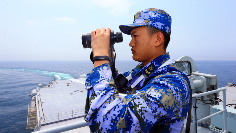 A PLA Navy sailor looks through binoculars atop the Shangdong aircraft carrier during sea trials