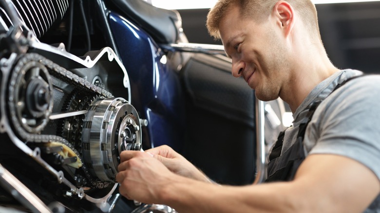A smiling mechanic fiddling with a motorcycle
