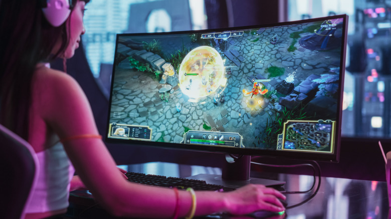 Person playing a PC game on a curved monitor at a desk