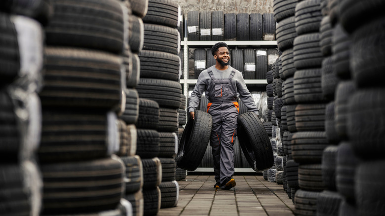 A person smiling and carrying tires while walking through a room full of tires.