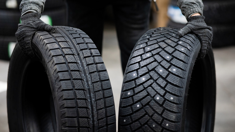 A person holding two different car tires next to each other.
