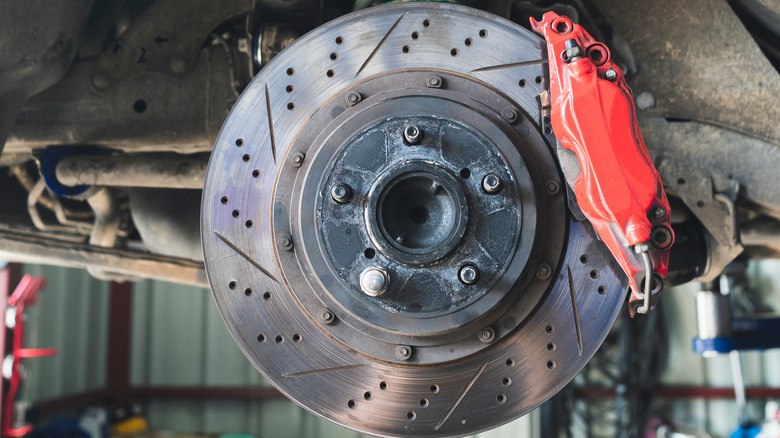 A close caption of a drilled and slotted brake rotor with a caliper