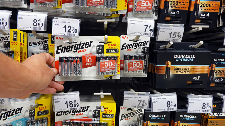 Hand choosing Energizer batteries from rack with mixed Duracell and Energizer options