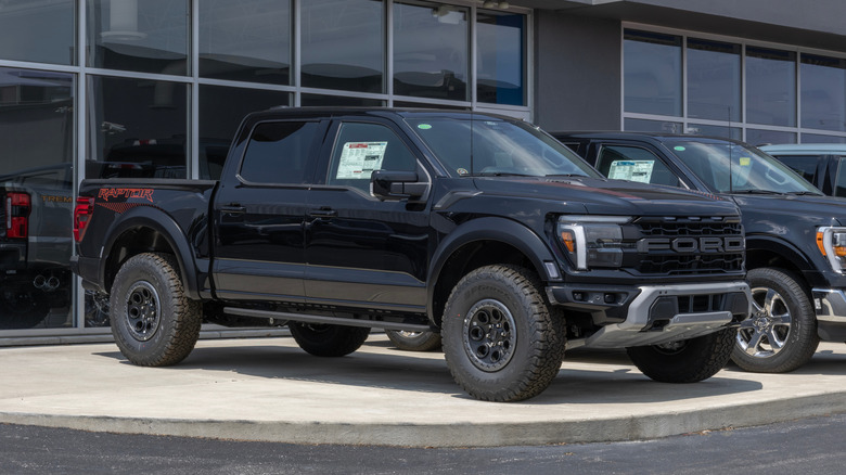 Front 3/4 view of black Ford F-150 Raptor parked outside of dealership.