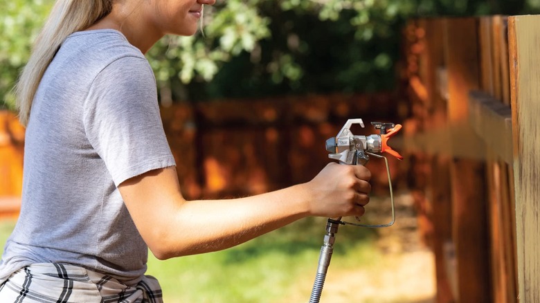 Woman using Graco Magnum 257025 Project Painter Plus to paint a wooden fence