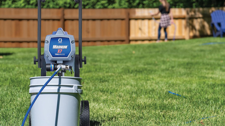 The Graco Magnum X7 on grass while a person in the background paints a fence