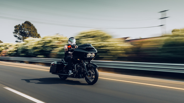 An action shot of a man riding a Harley-Davidson down a high way.