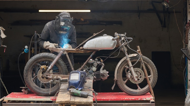 A man welding a custom motorcycle frame in a garage