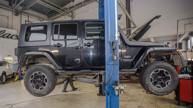 A Jeep Wrangler JK under repair, raised on a car hoist.