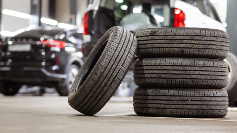 Tires stacked on top of each other, with one leaning against the stack inside a shop, with a blurred shop background.