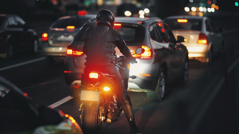 Motorbike rider waits in heavy evening traffic, vehicles on busy road with glowing headlights, ambient lights of the city