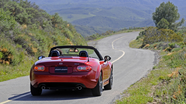 2015 Mazda MX-5 Anniversary Edition driving along narrow mountain pass, rear-view