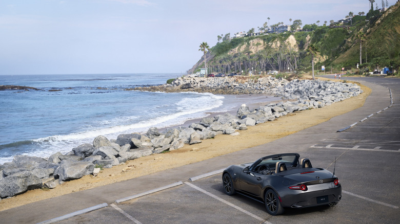 2024 Mazda MX-5 parked in front of rocky beach, rear-left 3/4 view