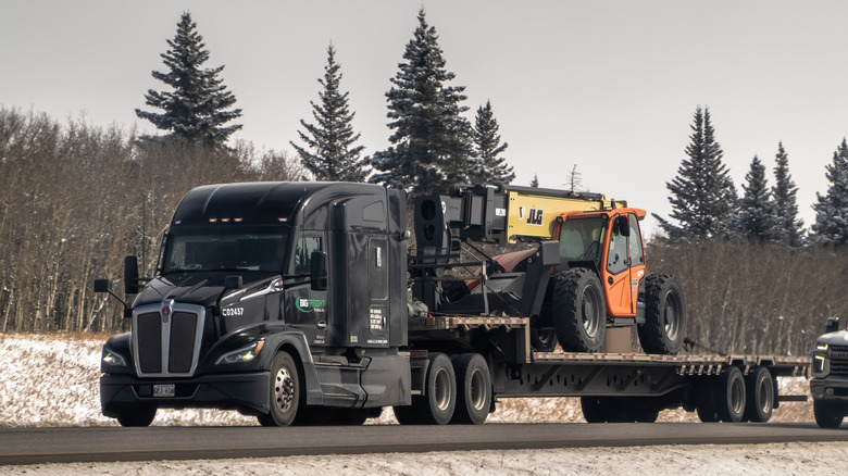 Black Kenworth T680 semi-truck hauling orange JLG telehandler