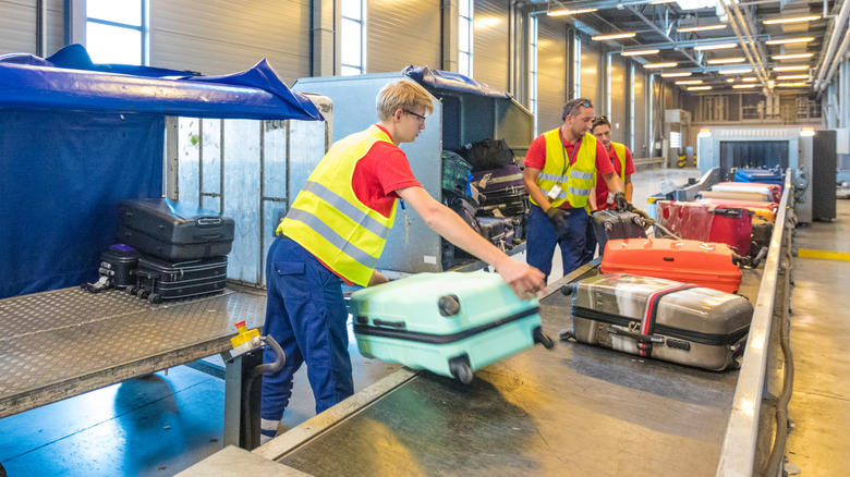 Ground crew unloading luggage from a baggage trailer.