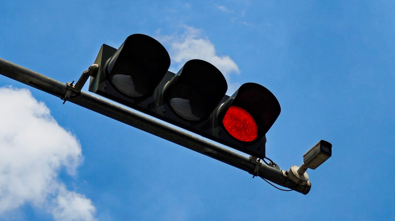 A red light camera on a horizontal traffic light pole against a blue sky.