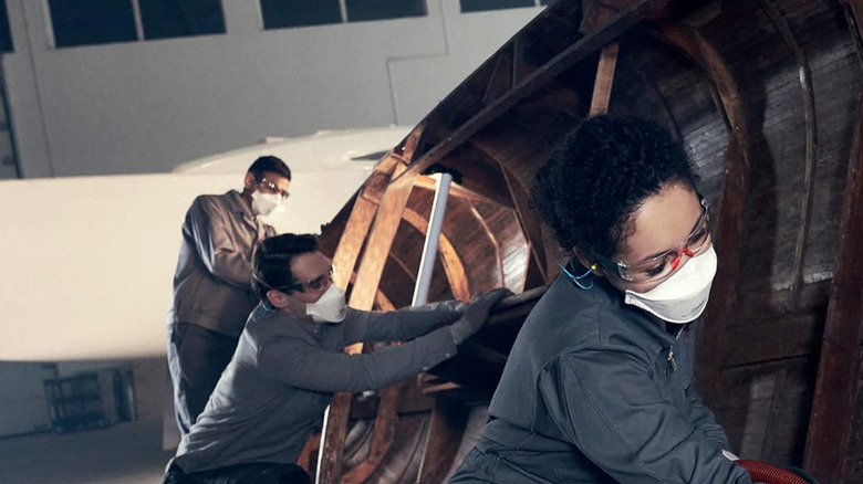 Two men and woman using orbital sanders on a wooden boat