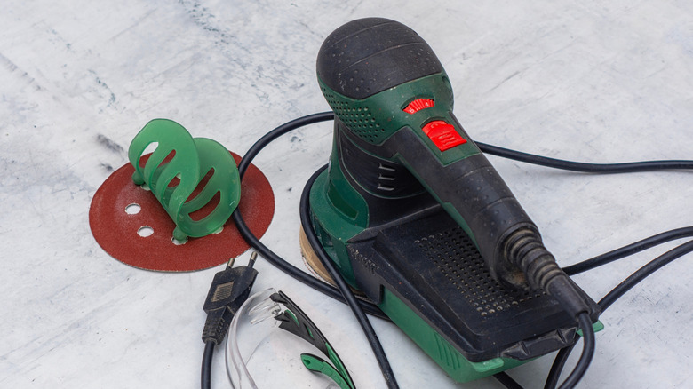 Orbital sander with sanding disc and goggles on a worktop