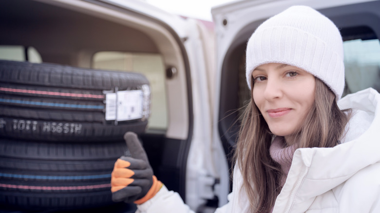 A woman in a white winter hat and coat giving a thumb's up while loading new snow tires into her vehicle