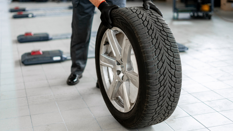 A man holding a tire and wheel inside a body shop