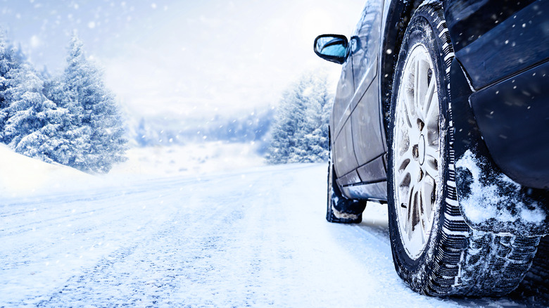 A close-up of a tire on a black vehicle driving on a snow-covered road during a snowstorm