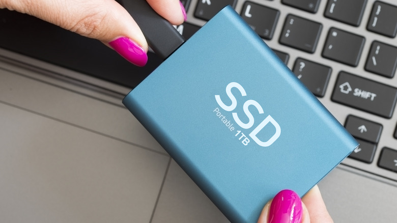 A woman's hand holdng a portble SSD with a notebook keyboard in the background