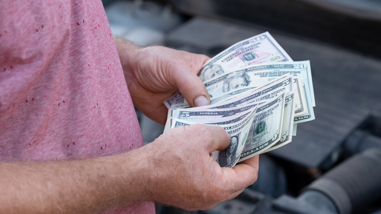 Man sorting through cash while standing next to car engine