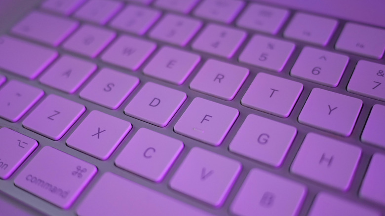 An Apple Magic keyboard under purple light.