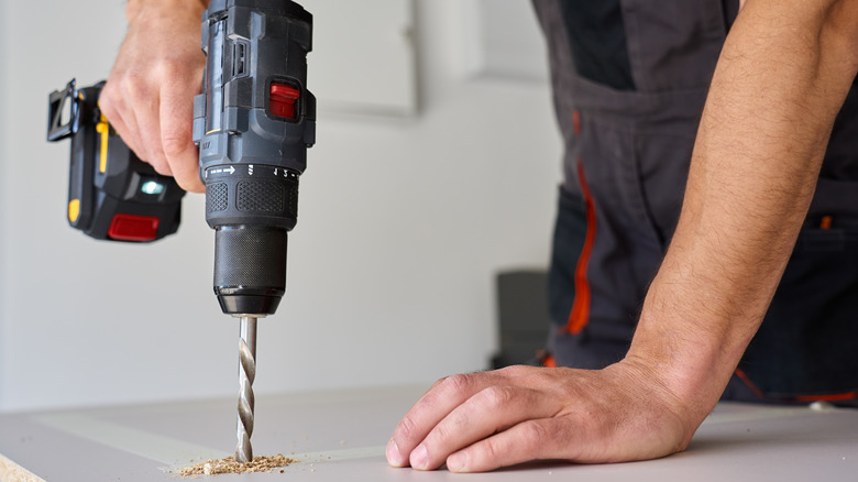 A man drilling into a wooden board with a power drill