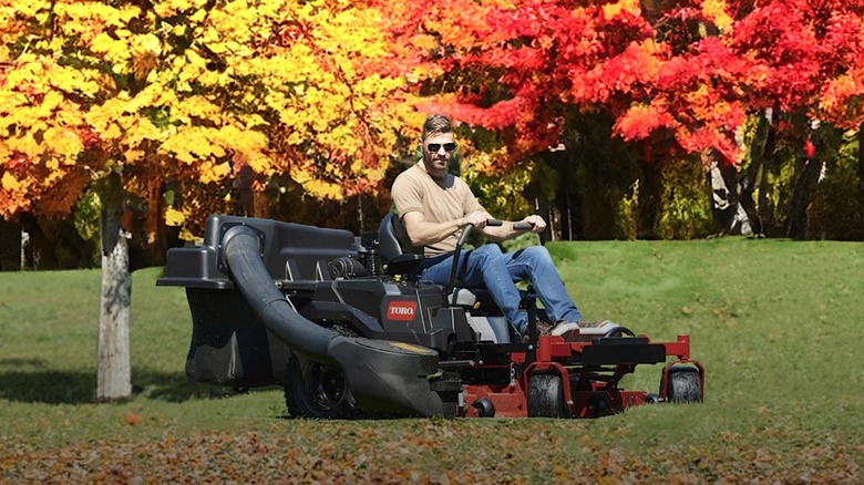 Person riding Toro lawn mower under fall foliage