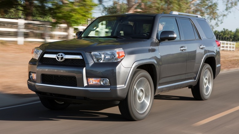 Fifth-generation Toyota 4Runner driving on a paved surface with trees and a white post-and-rail fence in the background