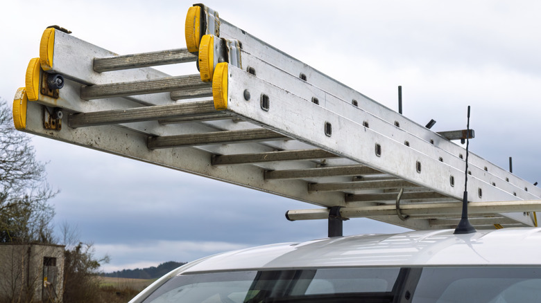 Aluminum extension ladder secured to roof rack on white contractor van