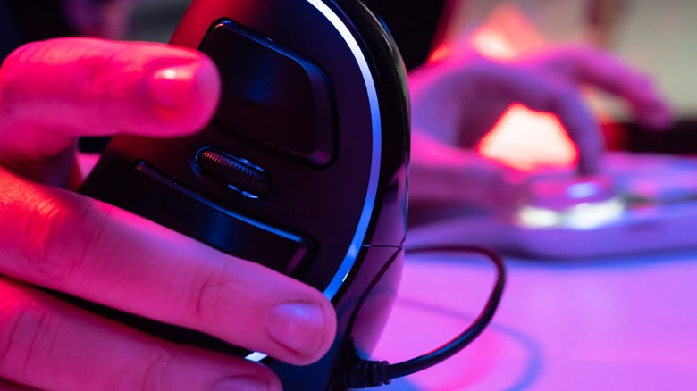 Black vertical mouse held in a neon-lit room with keyboard in the background