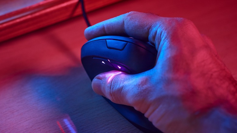 A male hand holding a black vertical mouse on an RGB-lit desk
